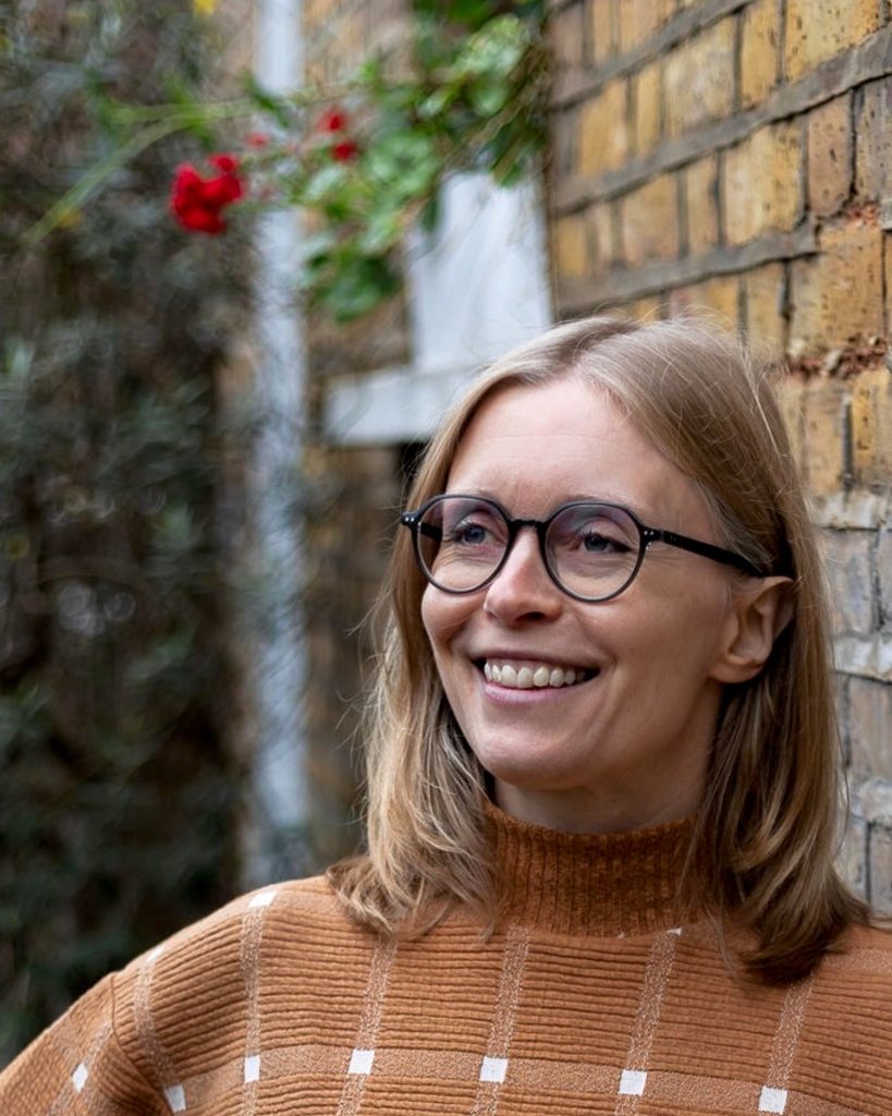 Gemma Rogers smiling outdoors beside a brick wall